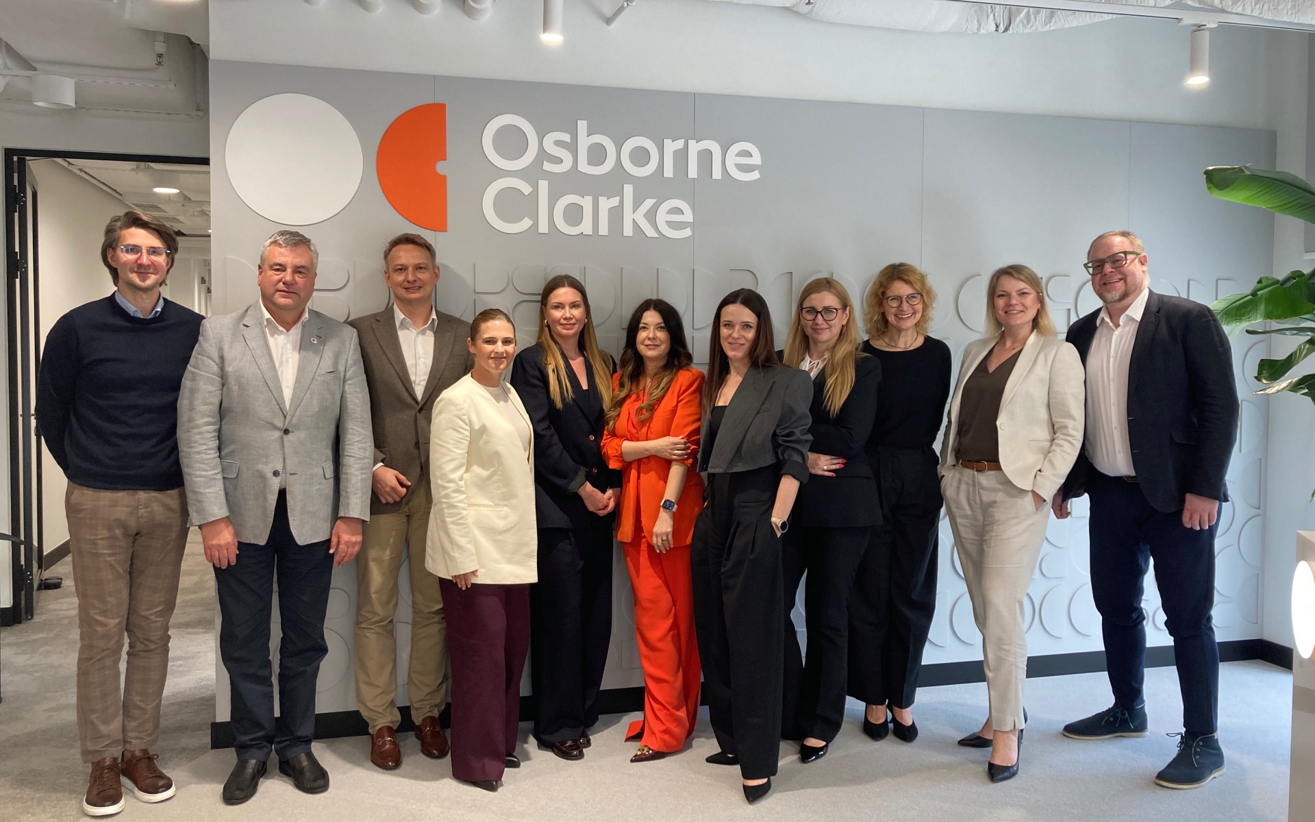 Eleven professionals in business attire posing in a modern office lobby with Osborne Clarke signage behind them.