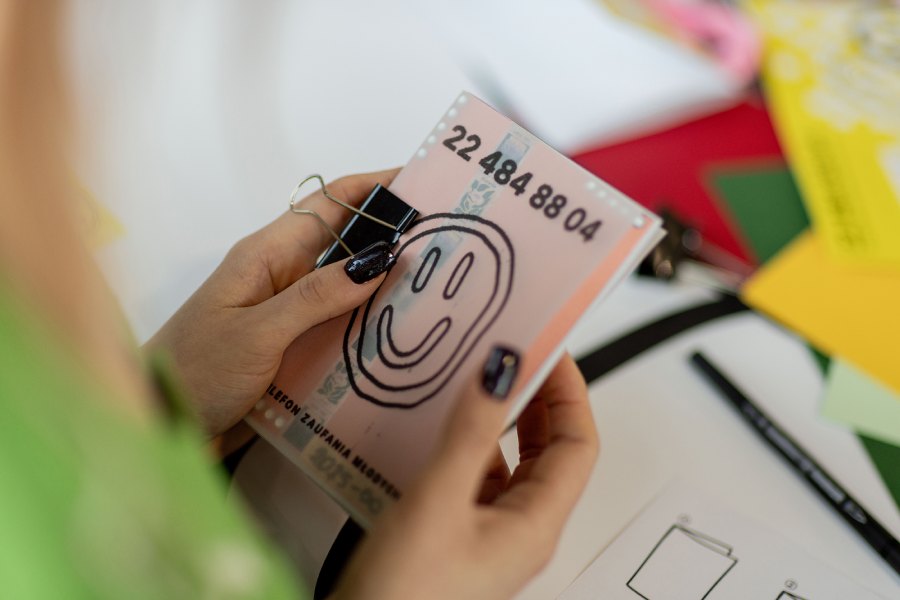 Close-up of a person’s hands clipping a pink banknote with a bold smiley drawing on it.