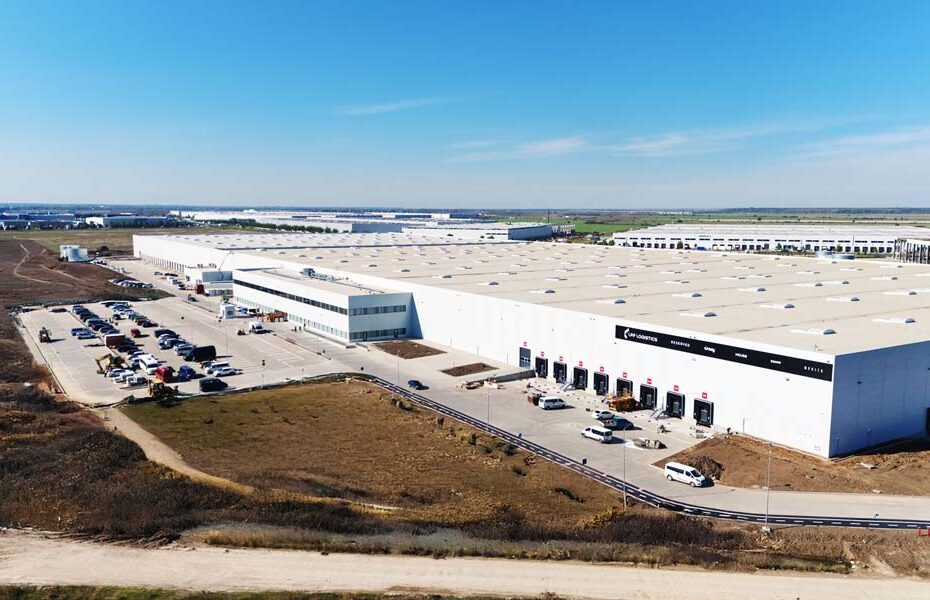 Aerial view of a large white logistics warehouse with loading docks and a parking lot.
