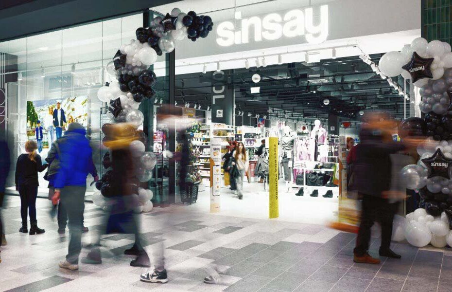 storefront entrance to a fashion shop with a black, white, and silver balloon arch, glass doors, and shoppers walking by outside and inside.