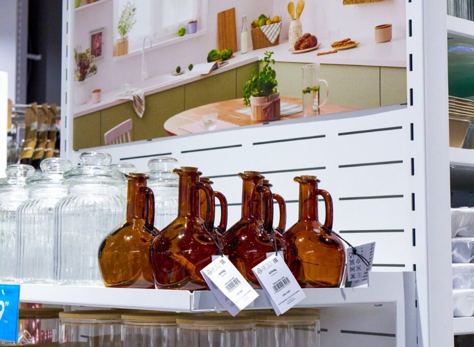 Row of brown glass bottles with handles on a store shelf beside clear glass jars and kitchenware displays
