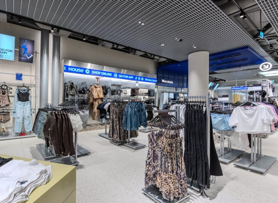 Interior of a clothing store with racks of outfits (leopard prints, denim) and bright overhead lighting.
