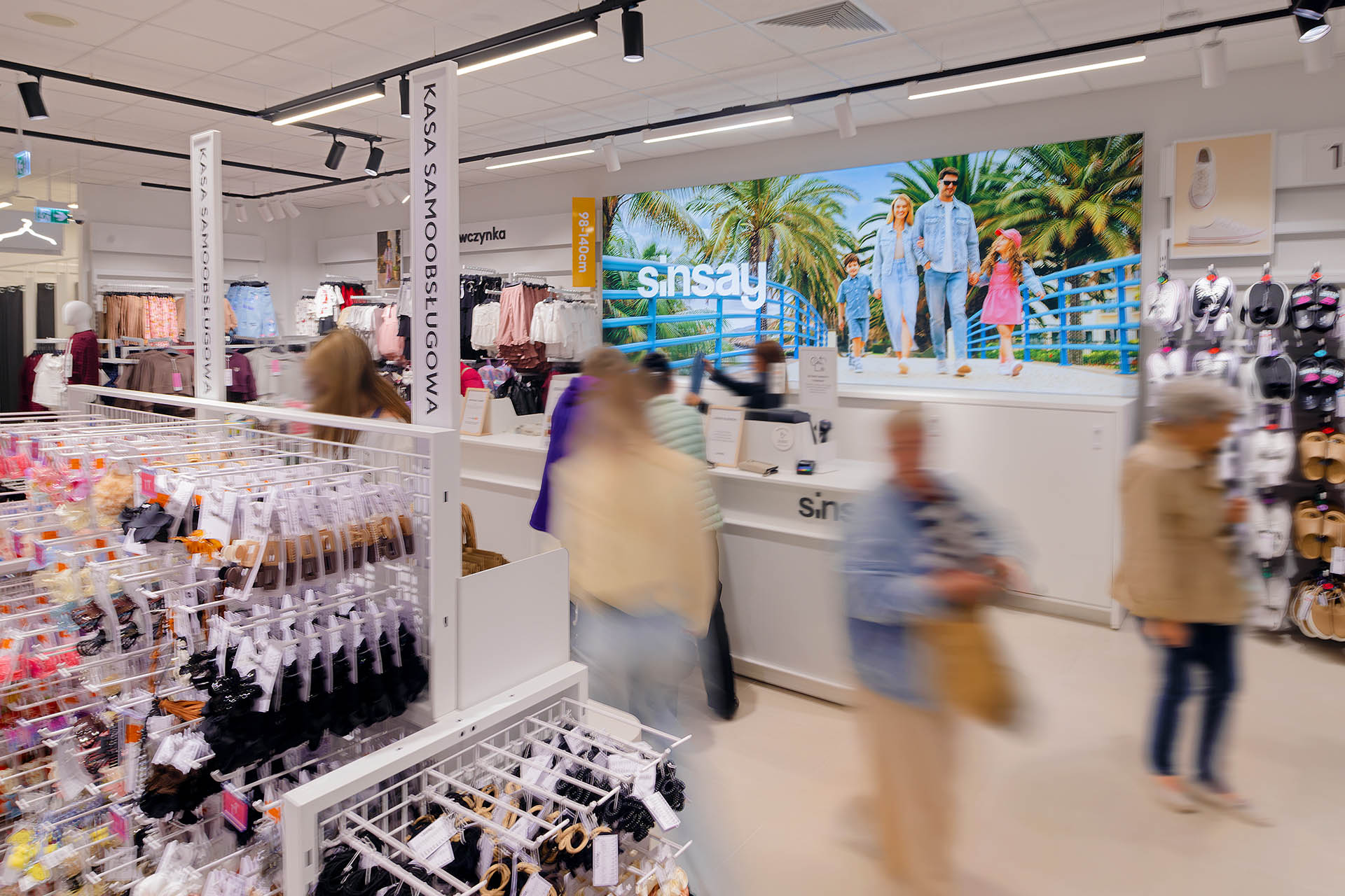 Interior of a fashion store with racks of clothes and a large tropical advertisement on the back wall.