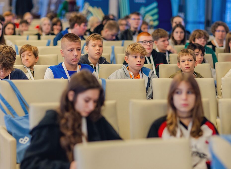Group of young students seated in an auditorium, wearing lanyards at a conference or event.